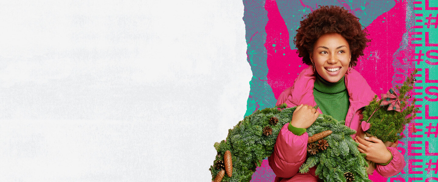 A smiling black woman in a pink jacket holds a Christmas tree and small plant with pink decorations