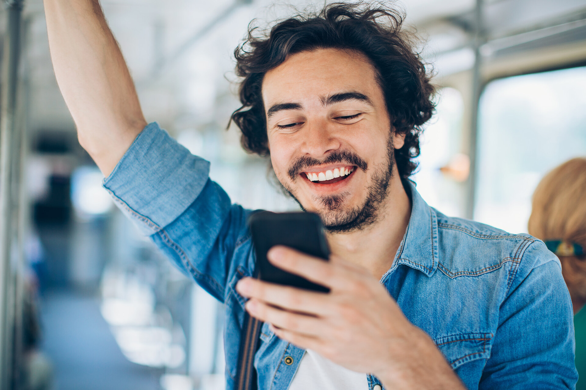 un hombre que viaja en autobús y lleva una camisa tejana sonríe mientras mira su teléfono