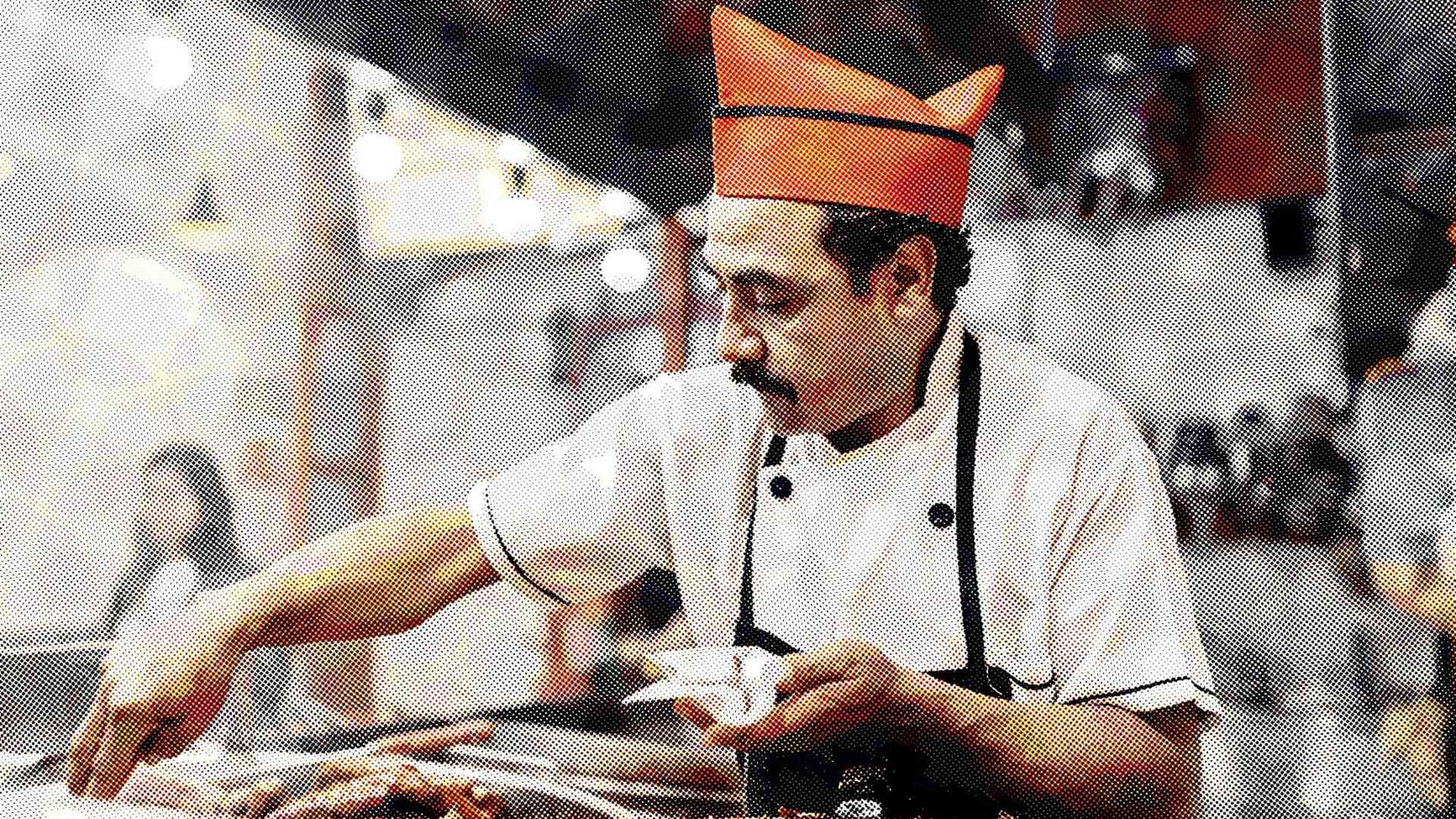Un chef que viste un uniforme blanco y un gorro naranja se inclina sobre la cocina de un restaurante y prepara comida