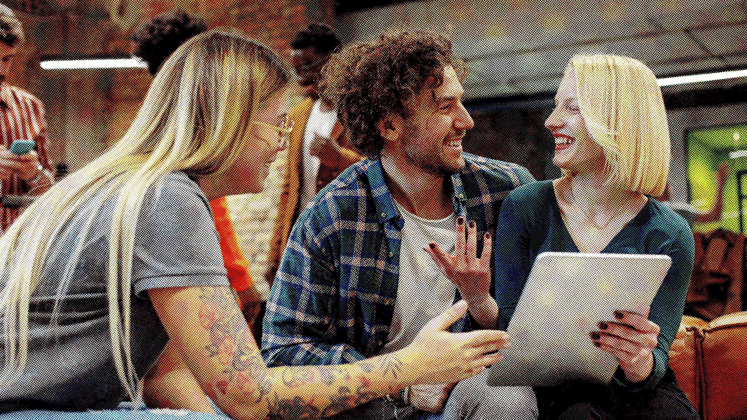 Trois employés sont assis et rient ensemble tandis que l'un d'eux tient un iPad. La femme à gauche est blonde et porte une chemise grise, l'homme au milieu est brun et porte une chemise à carreaux et la femme à droite est blonde et porte une chemise verte.